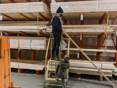 image of woman choosing wood in a hardware store lumber section by looking down the length of a board for warping image from blog post thats a introduction to the types of wood available for DIY projects