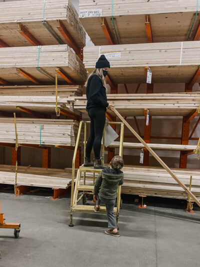 image of woman choosing wood in a hardware store lumber section by looking down the length of a board for warping image from blog post thats a introduction to the types of wood available for DIY projects